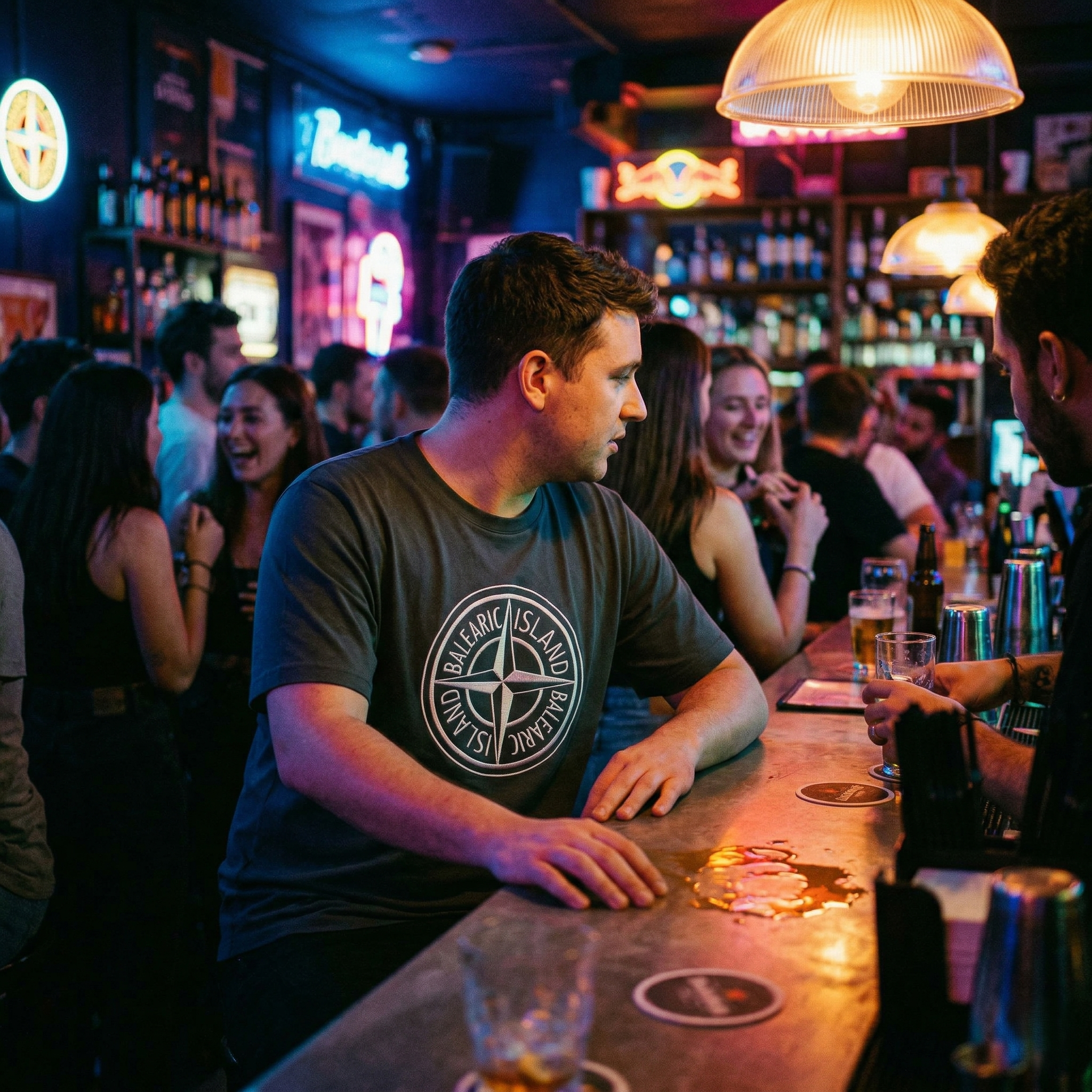 Balearic Blend T-shirt: Man in a dark, neon-lit bar wearing the charcoal Balearic Island compass graphic tee.
